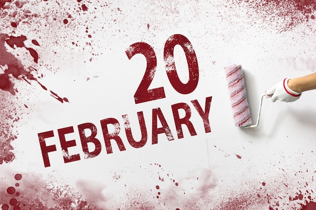 2월 20일. 매월 20일, 달력 날짜. 손은 빨간색 페인트로 된 롤러를 잡고 흰색 배경에 달력 날짜를 씁니다. 겨울 달, 올해 개념의 날.