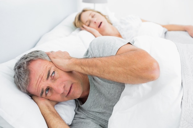 Fed up man blocking his ears from noise of wife snoring