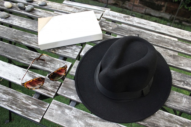 Foto cappello fedora, occhiali da sole e libro sulla giornata agghiacciante da tavola di legno all'aperto