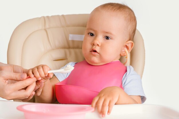 スプーンで赤ちゃんに餌をやる。幼児は食事をしながら椅子に座ります