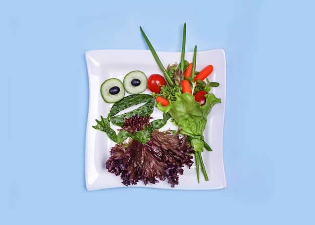 Feeding a child with a healthy vegetable salad with a funny frog made of cucumbers