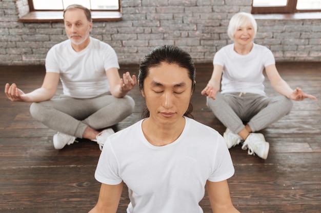 Feel solitude. positive delighted pensioner woman keeping smile on her face sitting behind her tutor while trying to meditate