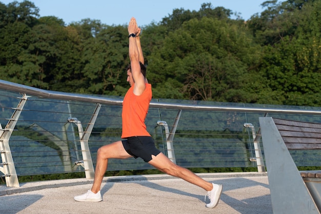 Feel the stretch in your hip. Man do crescent lunge stretch raising arms. Doing yoga or pilates exercise. Outdoor training and workout.