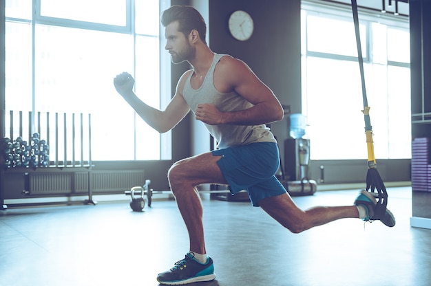 Feel your strength. Full-length side view of young man in sportswear exercising at gym