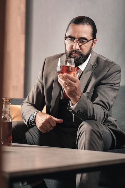 Feeling awful. Bearded dark-haired man drinking whisky while feeling awful after leaving his family