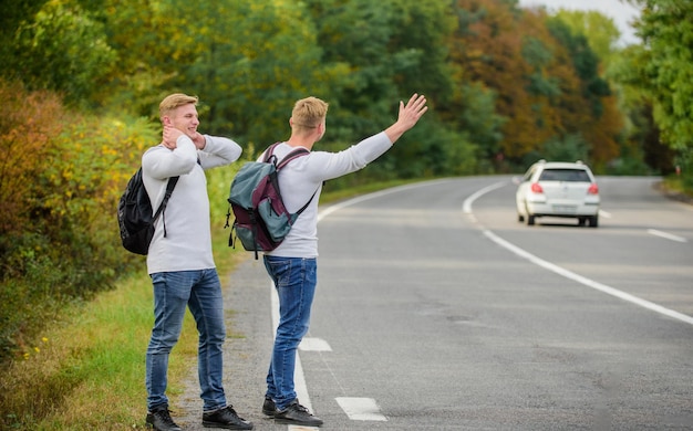 Feeling of being free twins walking along road stop car with thumb up gesture hitchhiking and stopping car with thumbs up gesture On the road Enjoying summer hike Looking for transport