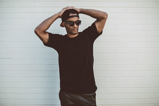 Feeling casual. Handsome young African man in casual clothes standing in front of the brick wall and holding hands behind head