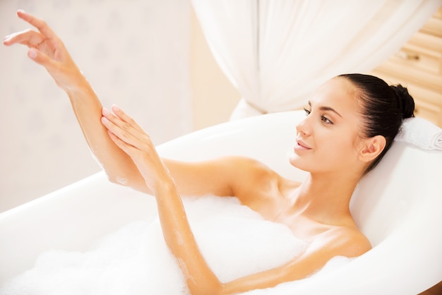 Feeling clean and fresh. Top view of attractive young woman touching her hand and smiling while enjoying luxurious bath