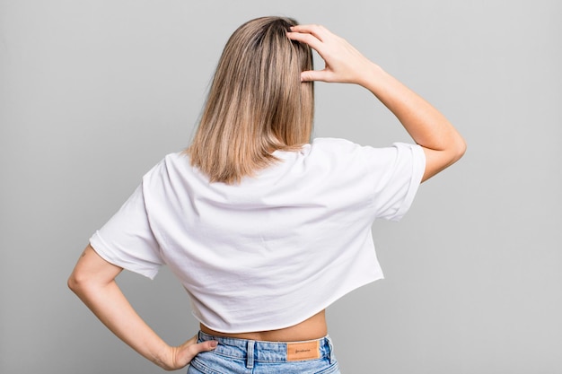 Feeling clueless and confused thinking a solution with hand on hip and other on head rear view