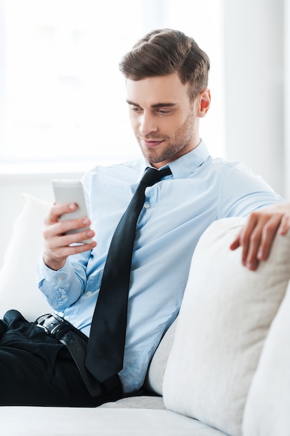 Feeling comfortable while doing business. Smiling young businessman holding mobile phone