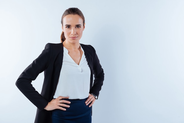 Feeling confident. Serious pleasant nice businesswoman putting her hands on hips and looking at you while feeling confident