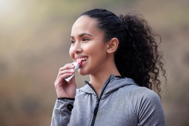 Sentirsi pieni di energia e pronti per la giornata. inquadratura di una giovane donna in forma che mangia una barra rosa mentre è fuori per un allenamento.