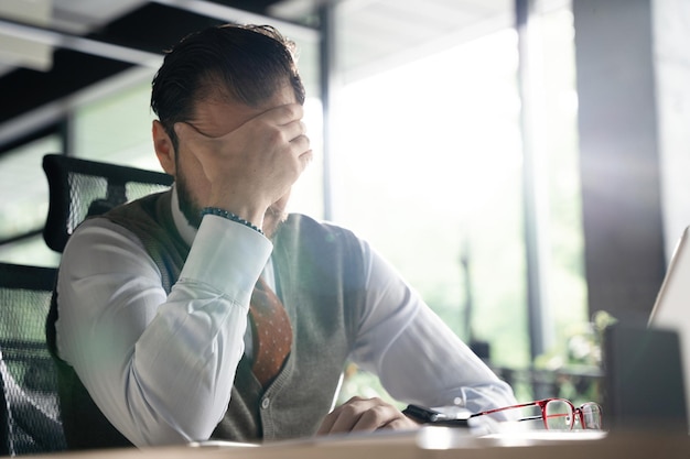 Feeling exhausted Frustrated middleaged beard man keeping eyes closed while sitting at his working place in office