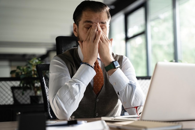 Photo feeling exhausted frustrated middleaged beard man massaging his nose and keeping eyes closed while sitting at his working place in office