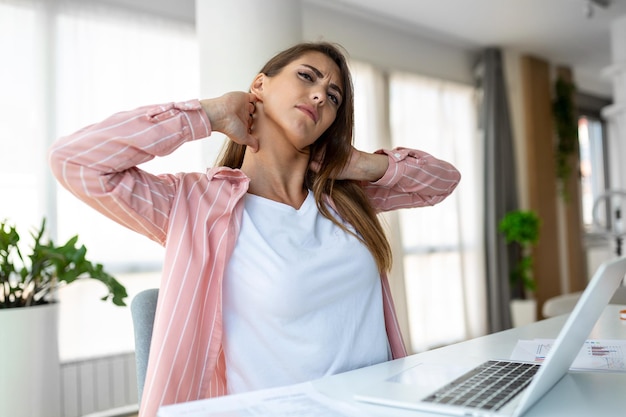 Sentendosi esausto donna frustrata che sembra esausta e si massaggia il collo mentre è seduta al suo posto di lavoro