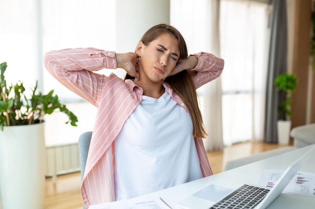 Feeling exhausted Frustrated woman looking exhausted and massaging her neck while sitting at her working place