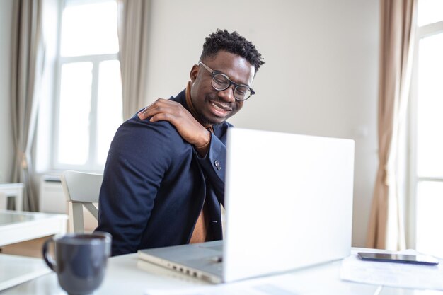 Feeling exhausted Frustrated young handsome man looking exhausted while sitting at his home and working on his laptop while massaging his neck Neck pain