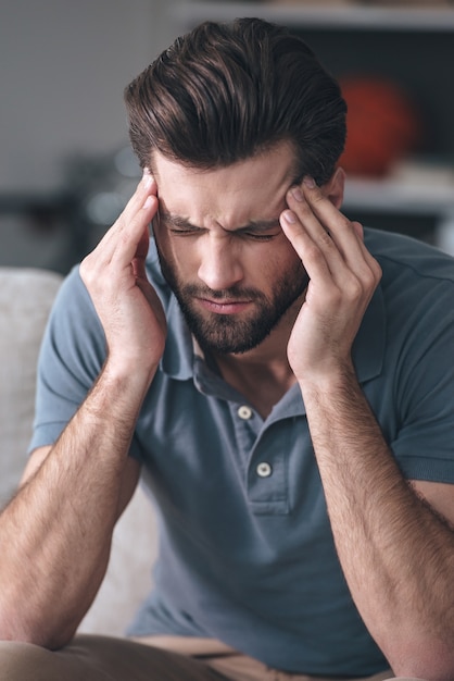 疲れた感じ。自宅のソファに座っている間、頭に触れて目を閉じて欲求不満の若い男