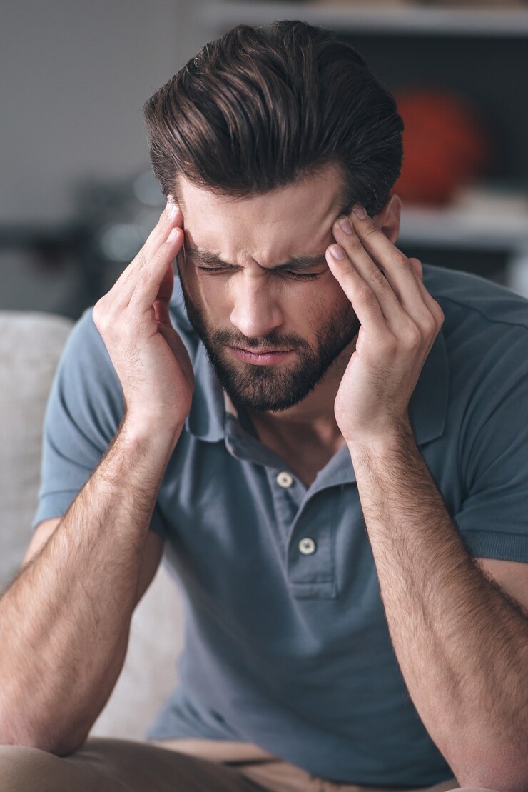 Photo feeling exhausted. frustrated  young man touching his head and keeping eyes closedwhile sitting on the couch at home