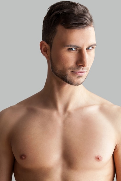 Photo feeling flirty. handsome young muscular man looking at camera while standing isolated on grey background