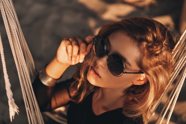 Foto sensazione di flirt. vista dall'alto di una giovane donna attraente che si aggiusta gli occhiali mentre è seduta su un'amaca sulla spiaggia