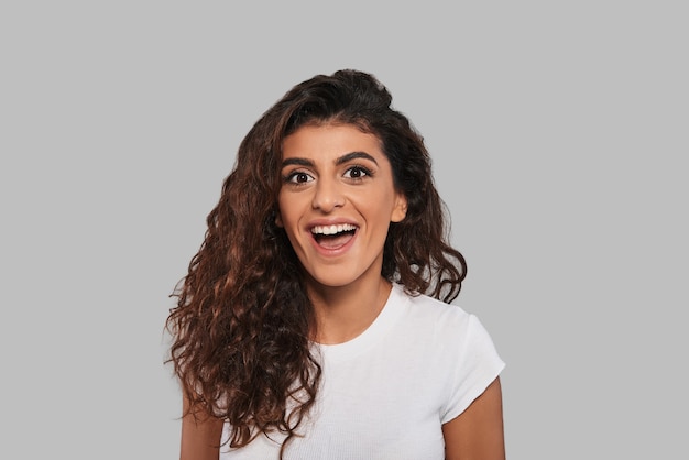 Feeling free to do anything. Surprised young woman looking at camera and keeping mouth open while standing against grey background