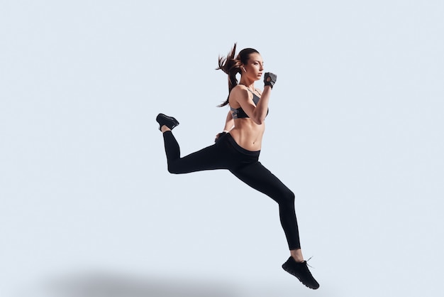 Feeling the freedom. Full length of attractive young woman in sports clothing exercising while hovering against grey background