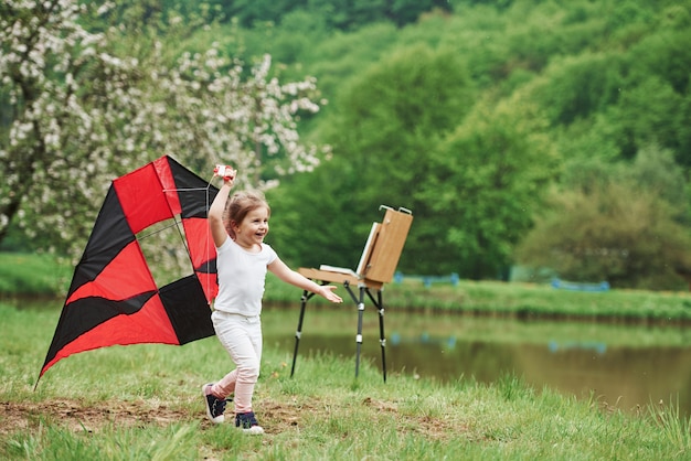 自由を感じます。屋外の手で赤と黒の色の凧で実行されている肯定的な女性の子供