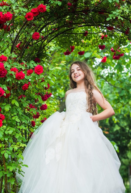 Feeling jubilant happy childhood beauty and fashion pretty kid smell rose flower spring and summer nature little girl in garden child enjoy blossom in park small angel for bride cute lady