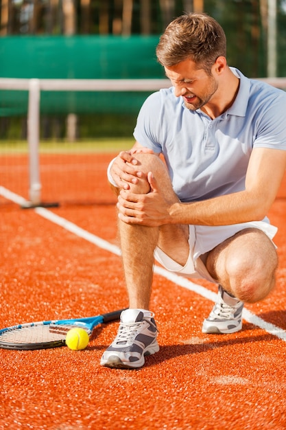 Sensazione di dolore al ginocchio. primo piano del giocatore di tennis che si tocca il ginocchio e fa una smorfia mentre è seduto sul campo da tennis