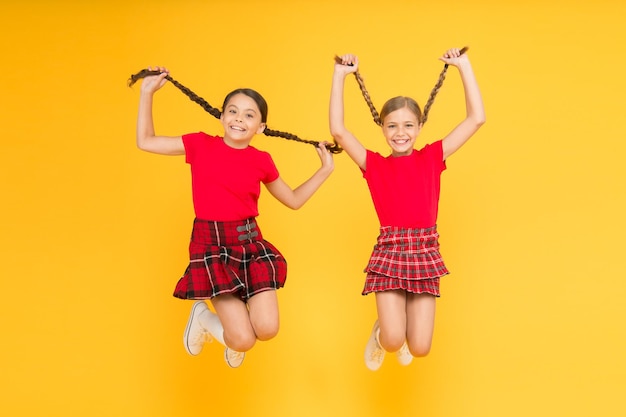 Feeling playful beauty look happy children on yellow wall childhood happiness trendy school uniform funny jump red fashion girls english style fashion happy little girls in checkered skirt