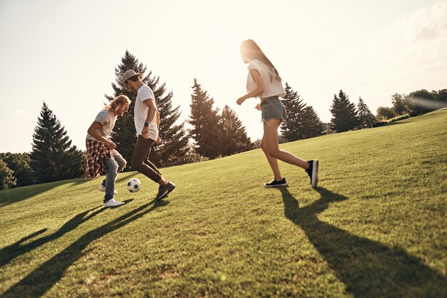 Photo feeling playful. full length of happy young people in casual wear playing soccer while running outdoors