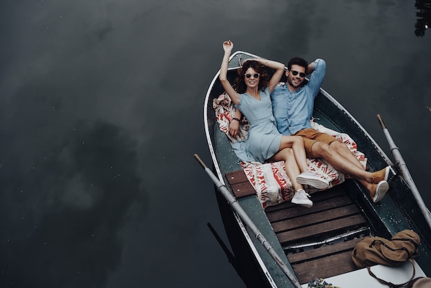 Ощущение игривости. Вид сверху красивой молодой пары, обнимающейся и улыбающейся, лежа в лодке