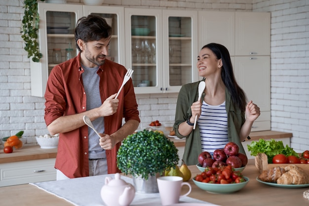 Feeling playful young happy family couple husband and wife having fun while preparing healthy food