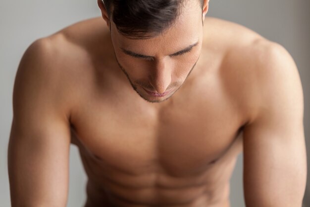 Feeling power inside. Handsome young muscular man looking down while isolated on grey background