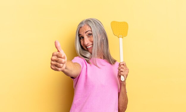 Feeling proud, carefree, confident and happy, smiling positively with thumbs up and holding a fly swatter