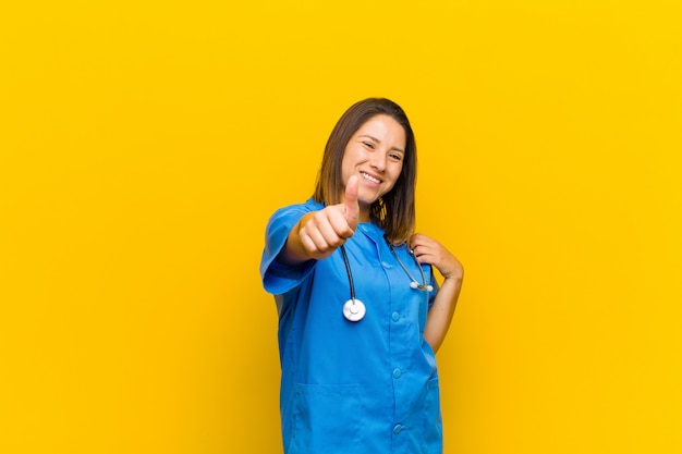 Feeling proud, carefree, confident and happy, smiling positively with thumbs up isolated on yellow wall