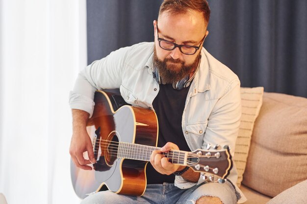 Feeling relaxed Man in casual clothes and with acoustic guitar is indoors