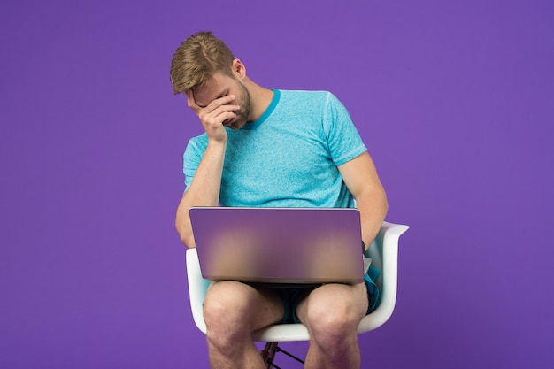 Feeling sick and tired. Frustrated young man covering face with hands while sitting with laptop. Man surfing internet on laptop. Guy working online. Man laptop surfing internet. Modern technologies.