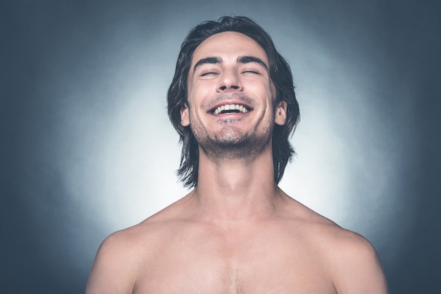 Feeling so happy. Portrait of young shirtless man looking at camera and smiling while standing against grey background