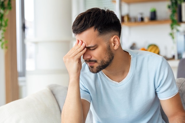 Sentendosi stressato giovane bello frustrato che si tocca la testa e tiene gli occhi chiusi mentre è seduto sul divano a casa