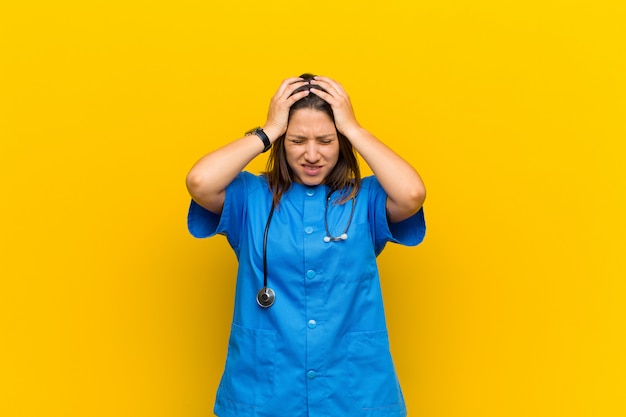 Foto sentirsi stressati e frustrati, alzare le mani alla testa, sentirsi stanchi, infelici e con emicrania isolata contro il muro giallo