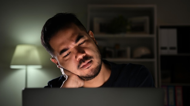 Чувство стресса и депрессии. Азиатский мужчина чувствует себя несчастным, напряженным и усталым, работая за компьютером поздно ночью дома