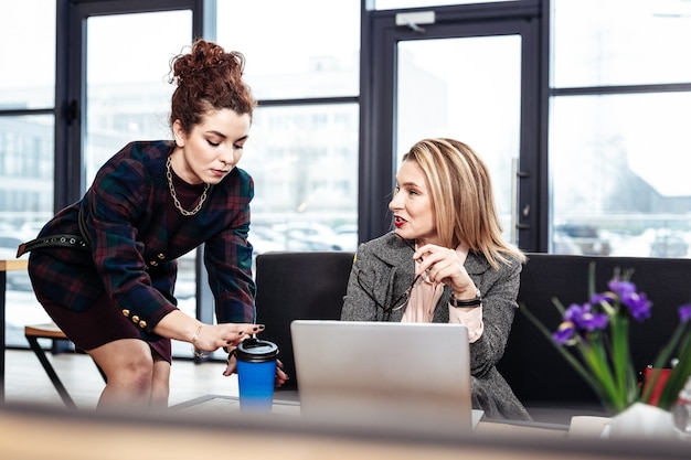 Feeling thankful. Blonde-haired female boss feeling thankful to her helpful secretary bringing some coffee