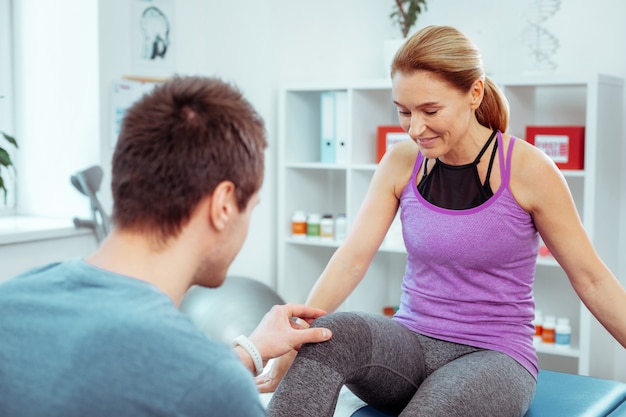 Feeling ticklish. Nice pleasant woman looking at her knee while feeling ticklish during medical checkup