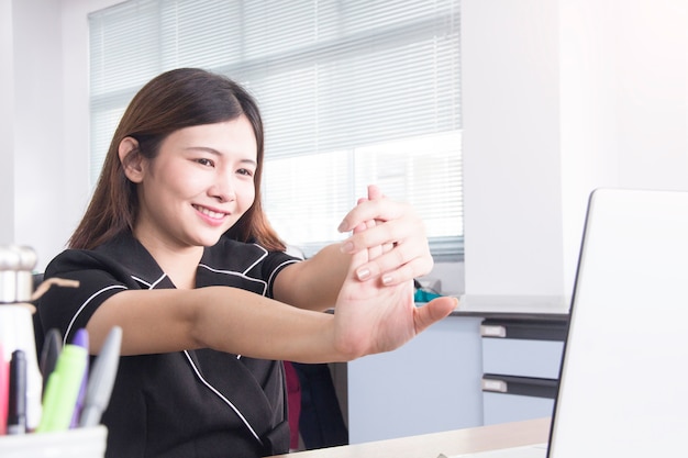 Foto sentirsi stanco. donna asiatica che massaggia il suoi braccio e spalla mentre sedendosi al suo posto di lavoro in ufficio.