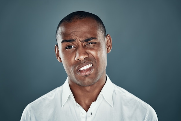 Feeling uncertain. Young African man in shirt looking at camera and frowning while standing against grey background