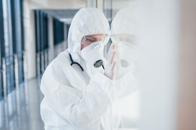 Feels bad and sick. Female doctor scientist in lab coat, defensive eyewear and mask standing indoors