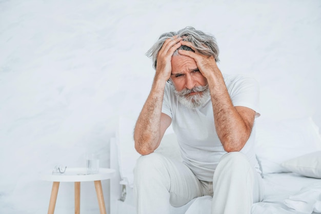 Feels sick On the bed Senior stylish modern man with grey hair and beard indoors