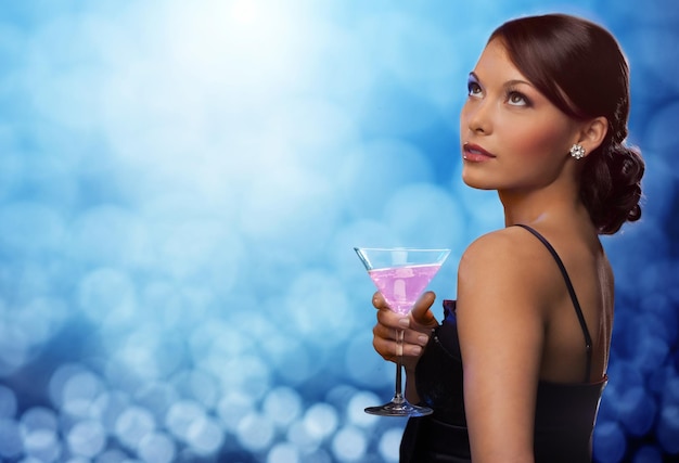 feest, drankjes, vakantie, luxe en feestconcept - glimlachende vrouw in avondjurk met cocktail over blauwe lichtenachtergrond